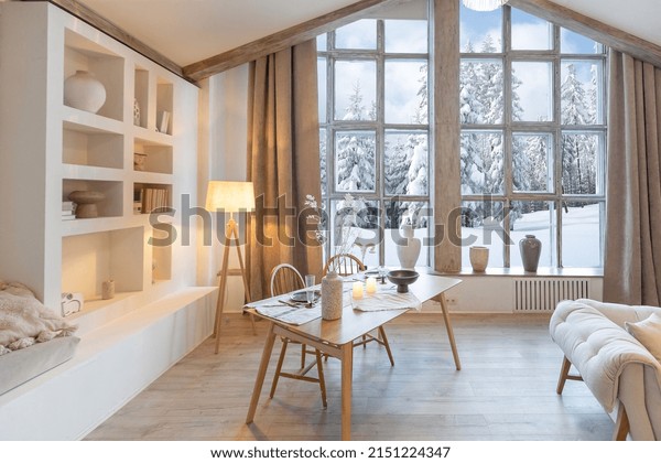 cozy warm home interior\
of a chic country chalet with a huge panoramic window overlooking\
the winter forest. open plan, wood decoration, warm colors and a\
family hearth
