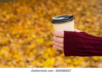 A cozy warm photo of a craft cup of hot coffee in hands against a background of fallen yellow leaves.