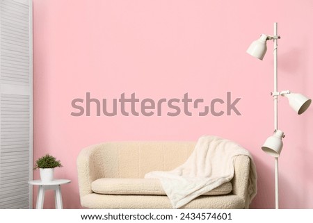Cozy white sofa, blanket and lamp near pink wall