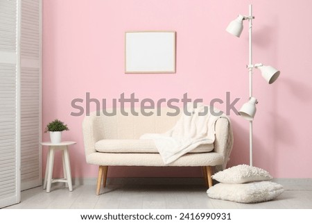 Cozy white sofa, pillows and lamp near pink wall