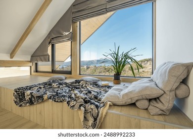 Cozy window nook with soft pillows and plaid invites relaxation. Natural light fills the space, showcasing a breathtaking view of a sea and hills through large windows. Sloped ceiling - Powered by Shutterstock