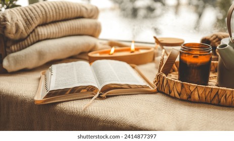Cozy winter photo, stack of sweaters, open Bible, tea and candle.