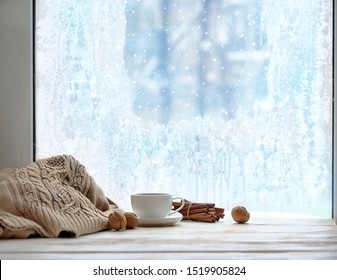cozy winter season. cup of tea or coffee, sweater, cinnamon, nuts, frozen window. home comfort in snowy cold weather. Christmas and New Year holiday background. 