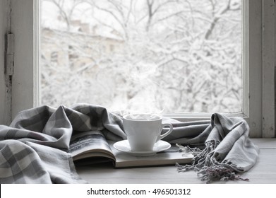 Cozy Winter Still Life: Cup Of Hot Coffee And Opened Book With Warm Plaid On Vintage Windowsill Against Snow Landscape From Outside.