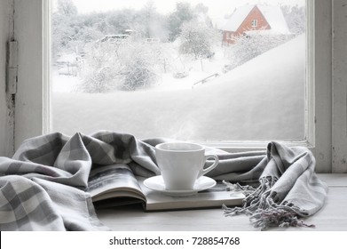 Cozy Winter Still Life: Cup Of Hot Coffee And Opened Book With Warm Plaid On Vintage Windowsill Of Cottage Against Snow Landscape With Snowdrift From Outside.