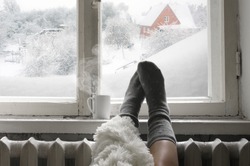 Cozy Winter Still Life: Woman Legs In Warm Woolen Socks Under Shaggy Blanket And Mug Of Hot Beverage On Old Windowsill Against Snow Landscape From Outside.