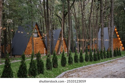 Cozy wooden A-frame cabins in forest with sunlight and outdoor seating area - Powered by Shutterstock