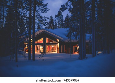 A cozy wooden cabin cottage chalet house covered in snow near ski resort in winter with the lights turn on, evening picture

