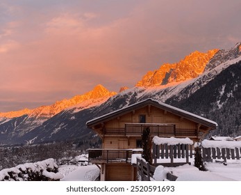 Cozy wooden hut nestled in the snow-covered Alps during a stunning orange sunset. The warm glow of the sun reflects off the snowy peaks, creating a tranquil winter wonderland. - Powered by Shutterstock