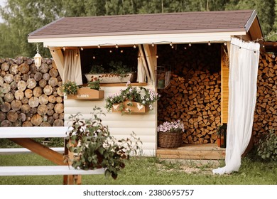 A cozy wooden shed with a lot of firewood in a tidy green yard with potted plants and flowers. Concept for home improvement, gardening, or rural lifestyle. Copy space on the left. - Powered by Shutterstock