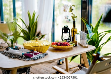 A cozy wooden table adorned with a vibrant yellow dish, fresh fruit, a decorative lantern, a bottle vase with white flowers, and a colorful woven cloth. - Powered by Shutterstock