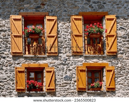 Cozy wooden windows with shutters and vibrant flowers on the stone wall in ‎⁨Lanuza village. Sallent de Gallego⁩, ⁨Huesca⁩, ⁨Spain⁩. Traditional vintage Spanish rural architecture.