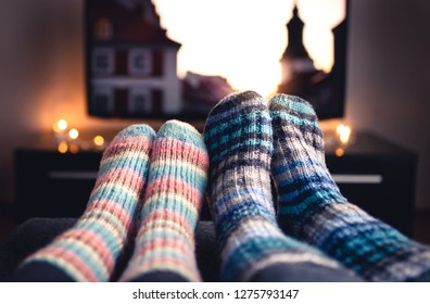 Cozy woolen socks. Couple watching tv in winter. Man and woman using online streaming service for movies and series. Relaxing quality time on sofa couch. People in warm home living room enjoying life.
