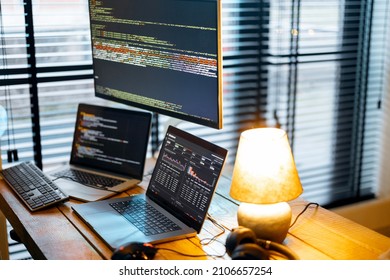 Cozy workplace with lapto and desktop computers with programming code on the screens. Programmer work table, Close-up view with no people