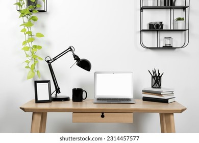 Cozy workspace with laptop, lamp and stationery on wooden desk at home