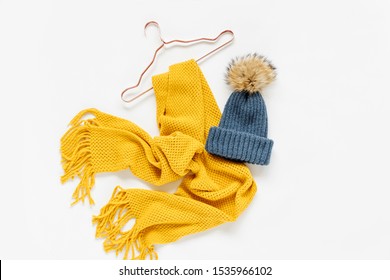 Cozy yellow scarf and blue hat with  hangers on white background. Women's stylish autumn or winter outfit. Trendy clothes collage. Flat lay, top view. 