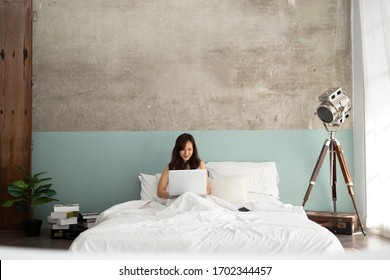 Cozy Young Asian Woman Freelancer Sit On Modern Bed And Typing Laptop With Lamp In Bed Room At Home. Work At Home Or Wfh.