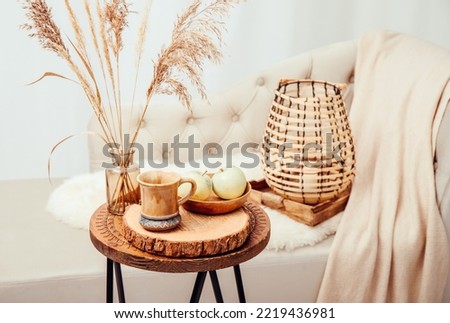 Cozycore or cottagecore concept, warm soft brown beige interior design objects. Cozy wool plaid on sofa, candle burning in wood lantern, tea cup on wood table. Warm color photo manipulation.