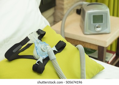 CPAP Headgear Mask With Air Tube Connecting To CPAP Machine In Bedroom