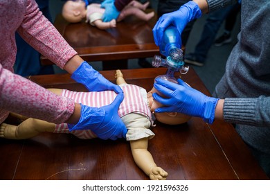 CPR practitioner examining airway passages on infant dummy. Model dummy lays on table and two doctors practice first aid. - Powered by Shutterstock