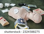 CPR training manikin near automated external defibrillator, wound care simulators, neck brace and bandages of floor in training room, medical equipment for first aid training and skills development