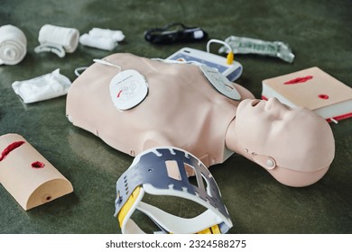 CPR training manikin near automated external defibrillator, wound care simulators, neck brace and bandages of floor in training room, medical equipment for first aid training and skills development - Powered by Shutterstock