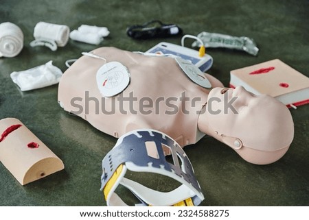 CPR training manikin near automated external defibrillator, wound care simulators, neck brace and bandages of floor in training room, medical equipment for first aid training and skills development