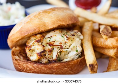 Crab cake sandwich on a bun with French fries, coleslaw and ketchup