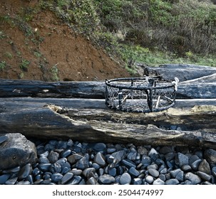 Crab pot washed ashore and landed on logs, driftwood and rocky beach. - Powered by Shutterstock