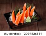 Crab sticks, or Surimi sticks with wasabi in black plate on wooden background.
