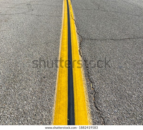 cracked asphalt road with bright yellow center\
stripe down the middle with black\
line
