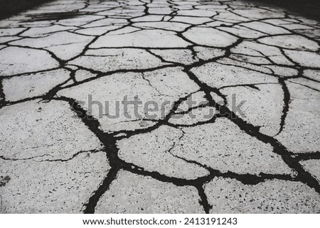 Cracked asphalt top view. Dry mud with black cracks. Grey ground background top view. Global warming problem, disaster. Aftermath of the earthquake. 