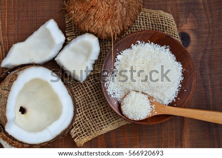 Cracked coconut and grated coconut flakes on wooden plate over dark wooden table, overhead view
