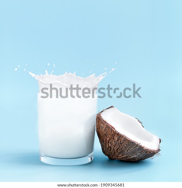 Cracked coconut with splashes of milk in glass\
on blue background