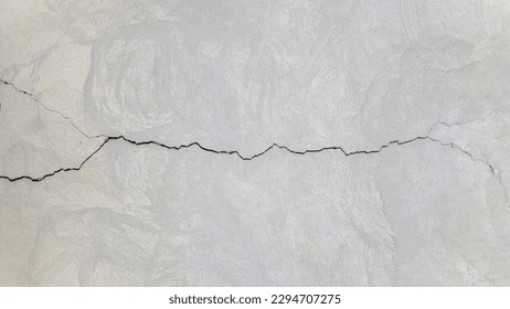 Cracked concrete surface covered with gray cement mortar. Destruction after the earthquake. Rough long winding crack in the wall. Copy space. Texture background. Repair, construction of buildings