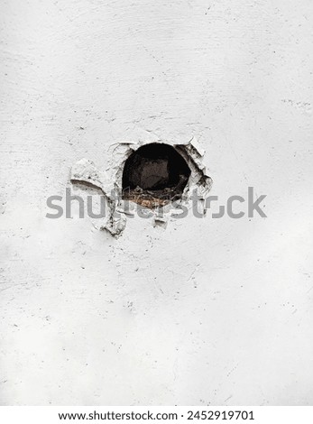 A cracked hole in an old white cement wall was caused by drilling to install pipes for a home water system installation.