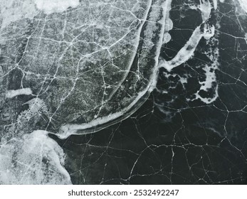 Cracked ice surface with intricate, web-like patterns over dark green water, highlighted by jagged white frost along the edges. - Powered by Shutterstock