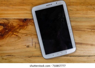 Cracked LCD screen of tablet on rustic table.