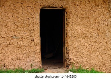 A cracked mud house exterior wall with a darkened doorway - Powered by Shutterstock