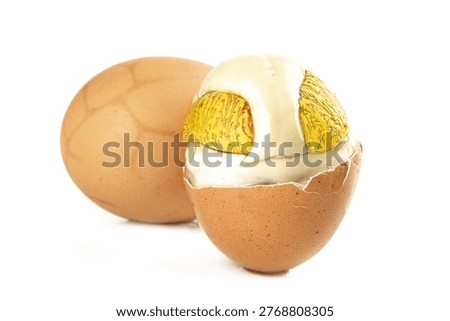 Cracked open brown egg shell revealing golden foil-wrapped chocolate candies inside, creative food concept on white background