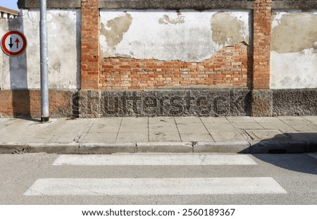 Cracked plaster wall with bricks exposed in the middle. Roadsign on the left, sidewalk,street and crosswalk in front. Grunge background for copy space.