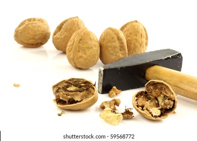 a cracked and some whole  walnuts with a hammer on a white background