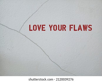 Cracked wall with red text LOVE YOUR FLAWS, concept of positive self talk, learning self love and boost confidence, appreciate and accept our own flaws