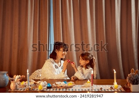 Cracking eggs for a good luck. Smiling happy mother and her little daughter holding painted Easter eggs. Home celebration. Concept of holiday, Easter, family, motherhood and childhood, traditions