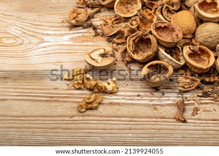Cracking nuts on a wood table close up. Macro photo of crushed walnuts, broken walnut shells with kernel, nutshell heap, fresh raw healthy food top view