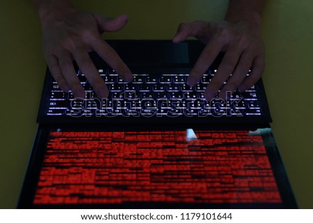 cracking privacy data. hacker man hands typing on back lit keyboard. laptop monitor screen displaying block of red binary bit data. computer on a desk. computer crime and hacking concept.