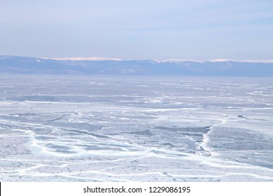 Cracks on the surface of the blue ice. Frozen lake in winter mountains. It is snowing. Lake Baikal. Winter