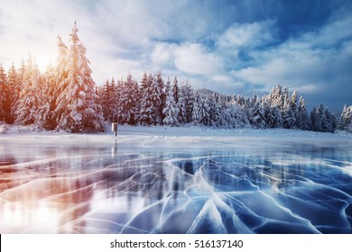 Cracks the surface the blue ice  Frozen lake in winter mountains  It is snowing  The hills pines  Carpathian Ukraine Europe 