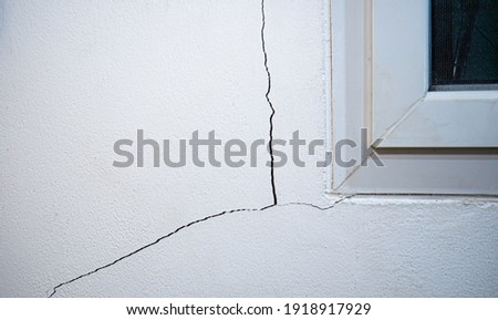 Cracks on the wall at the house or residence. The crack in the cement wall at the window sill, caused by the subsidence of the ground, caused a slit at an oblique angle.