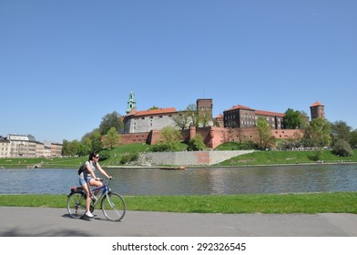 CRACOW, POLAND - JULY 27 - Tourist On Bike Admiring Royal Castle Over The Vistula River In On July 27, 2012 In Krakow (Cracow), Poland